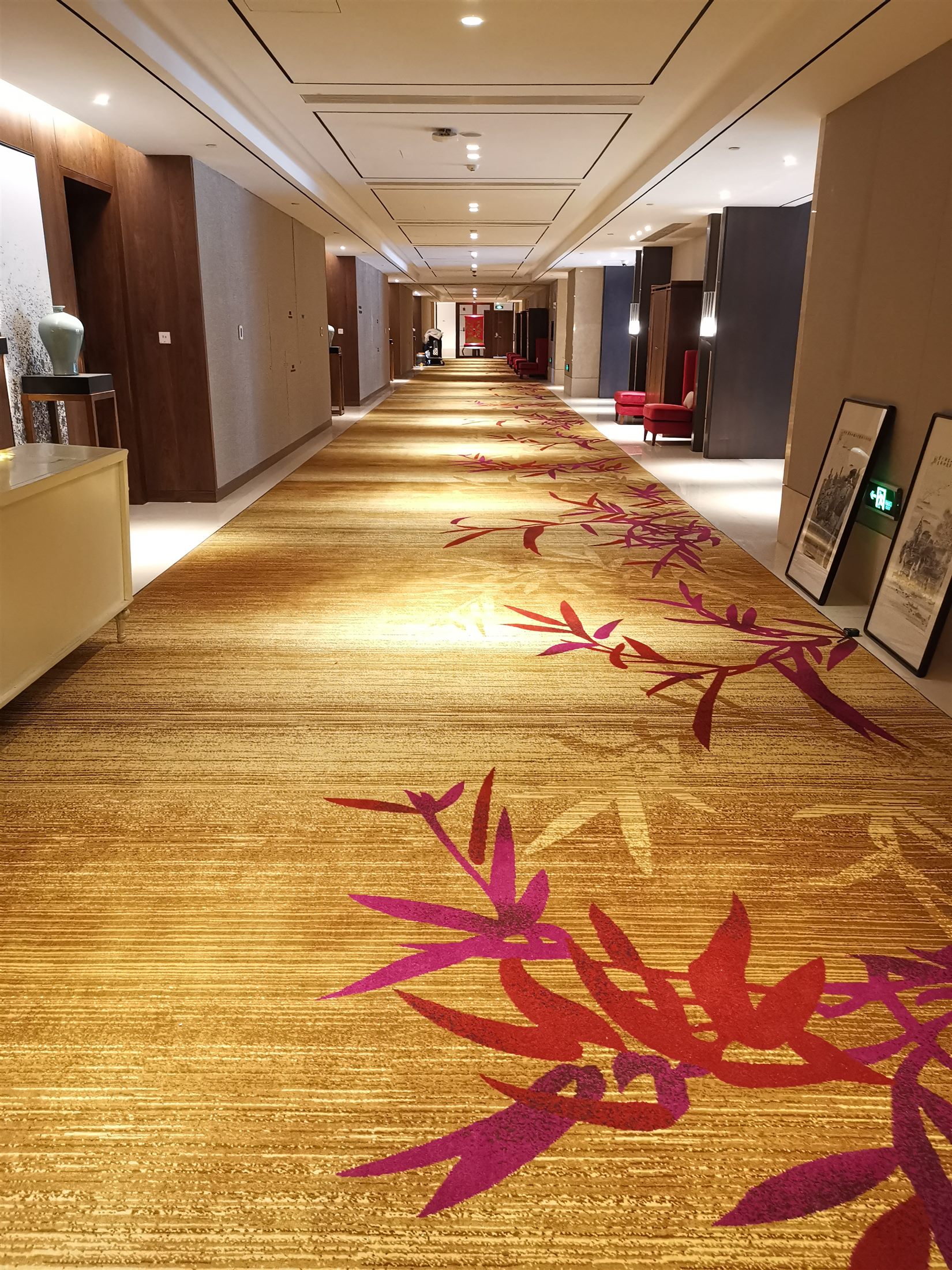 Long hotel corridor with a gold carpet and magenta botanical linework